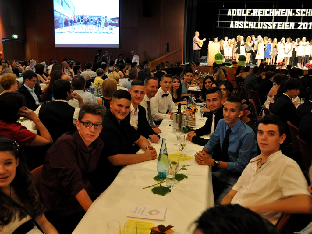 Jugendliche sitzen an der Tafel, im Hintergrund die Bühne.